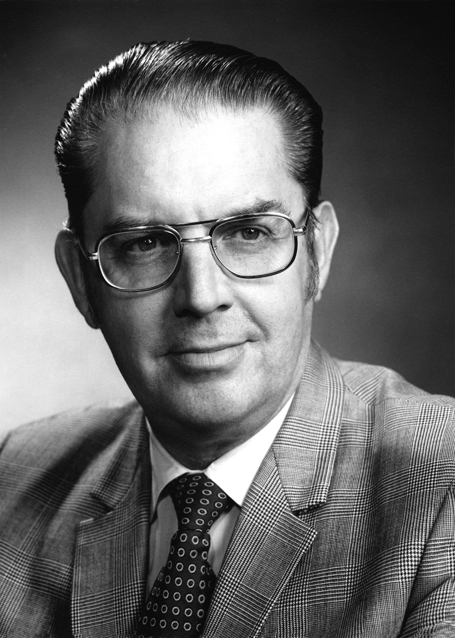 Howard Tanner wearing glasses, a suit, and tie